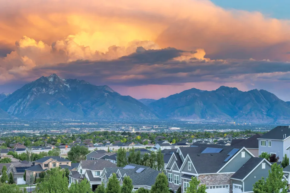 View of residential neighborhood with large homes with tall mountains and cloudy sunset sky in background in Salt Lake City, Utah.